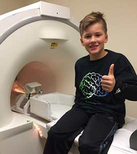 Photo of a boy sitting on table preparing for his MRI scan.